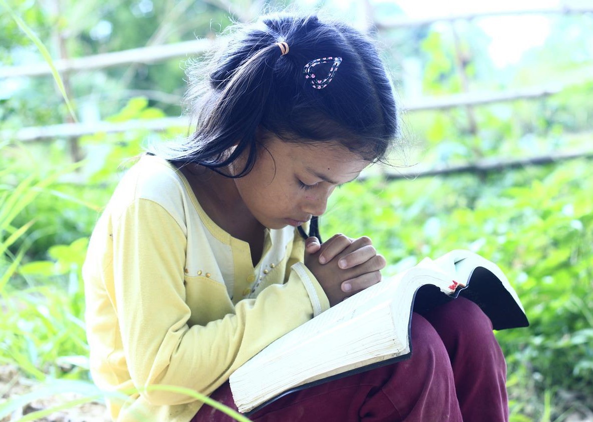 Young girl reading Bible and praying, showing devotion to God and pure and undefiled religion.