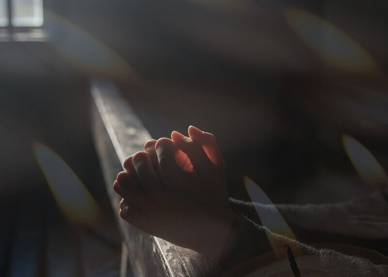 Person praying in a darkened church sanctuary, wondering how God will answer their prayer