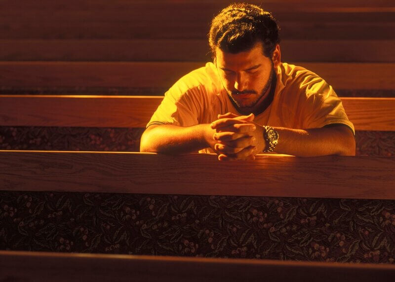 Man in church pew praying to God with faith, hope, and love.