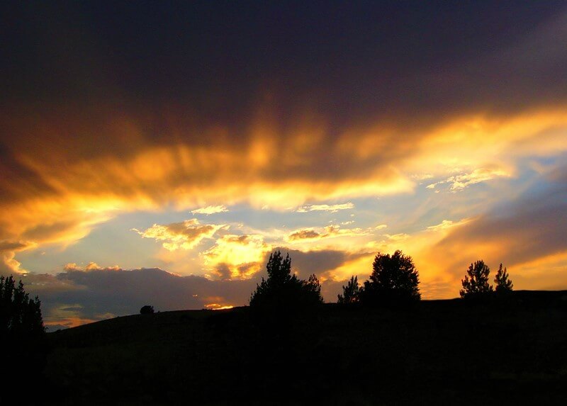 Glorious rays from the setting sun over a dark landscape of land and trees, suggesting the believer's hope of receiving a spiritual inheritance in the future